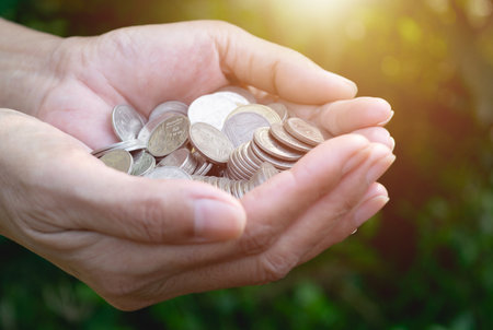 hand holding coins with tree under sunshine and gardening green background.の写真素材