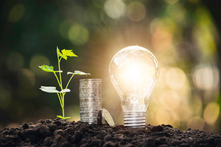 Light bulb with coins and young plant  for saving money,financial,business or energy concept put on the soil in soft green nature background.の写真素材