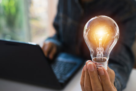 Business woman holding light bulb on the desk in office and using  computer in ...