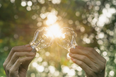 Hand holding light bulb in nature on green background for energy concept.の写真素材