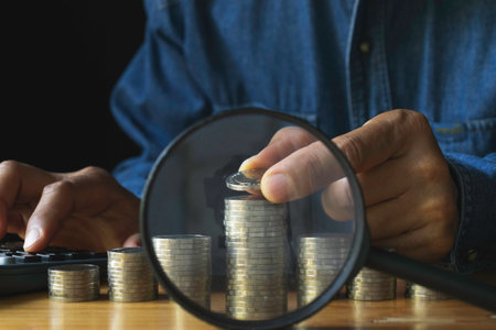 Business man putting  a coin on coins stack and magnifying glass for saving bank and account for his money all in finance accounting concept.の写真素材