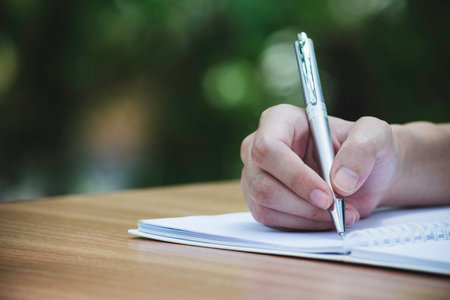 Closeup hand of woman writing notebook for her work in park background.