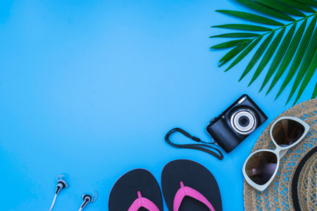 Flat lay, top view with hat,slippers,camera,
sunglasses,earphone and green leaf tropical palm for travel,summer and holiday concept on soft blue background.の写真素材