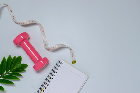 Healthy object on table with dumbbells,notebook,green leaves,measuring for sport or exercise concept on blue background.の写真素材