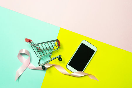 Top view,flat lay smartphone shopping cart with pink ribbon to decoration for shopping and e-commerce concept on pastel colorful background.の写真素材