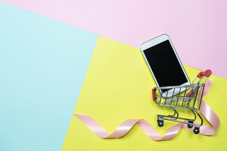Top view,flat lay smartphone shopping cart with pink ribbon to decoration for shopping and e-commerce concept on pastel colorful background.の写真素材