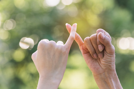 Closeup two person hook each other's little finger on nature background.の写真素材