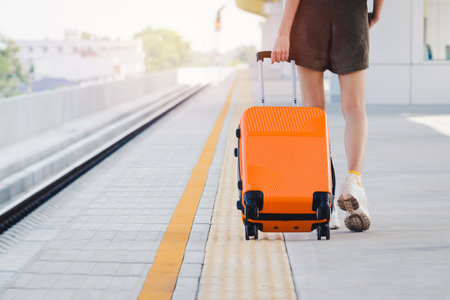Woman tourist with orange suitcase waiting the train at train station background. travel, tourist, vacation concept.の写真素材