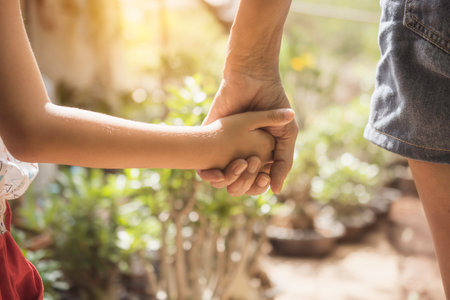 Closeup female holding hand of child standing in garden with sunny on background.の写真素材