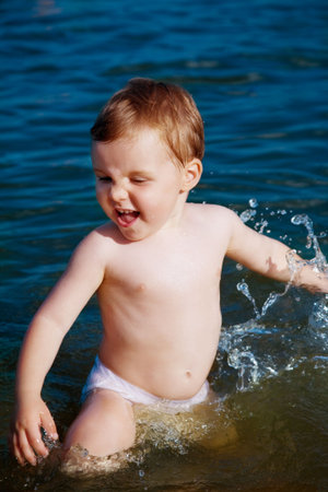 Little child laughing in the spray of waves at waterの写真素材
