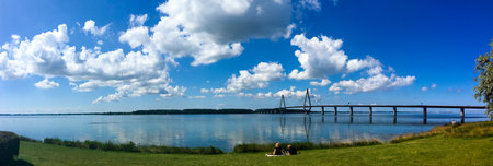 A loving couple having a summer picnic next to the water and the Faroe Bridges in southern Denmark.のeditorial素材