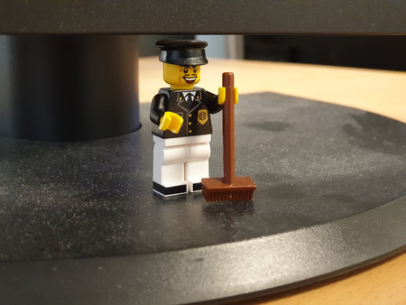 A custom made LEGO figure, dressed as a guard or maintenance worker, holding a brown broom, sweeping the dust, in an office setting.のeditorial素材