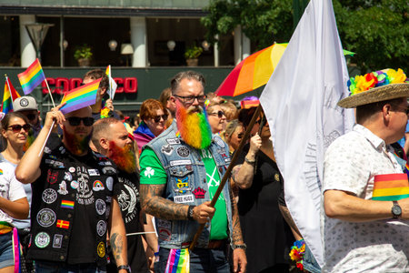 MalmÃ¶, Sweden - July 20, 2019: A masculine man with tattoos and glasses has colored his full beard in the colors of the rainbow as he is participating in the gay pride parade in MalmÃ¶, Sweden.のeditorial素材