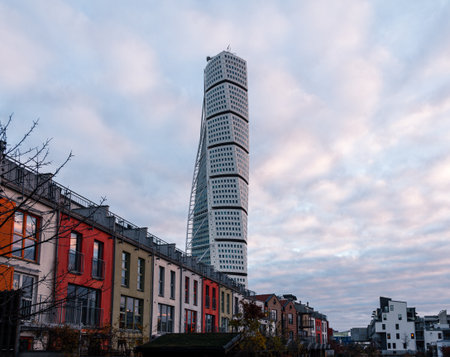 MalmÃ¶, Sweden - November 25, 2018: Turning Torso stands tall behind colorful buildings on a windy and cold winter day with sky full of fluffy cloudsのeditorial素材