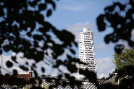 MalmÃ¶, Sweden - August 10, 2018: The white facade of the ultra modern skyscraper Turning Torso is seen between the leaves in a parkのeditorial素材