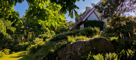 SkÃ¤ret, Sweden - June 18, 2017: An old cozy cottage is embedded into a beatiful sunlit garden with wild plants and trees and rocks.のeditorial素材