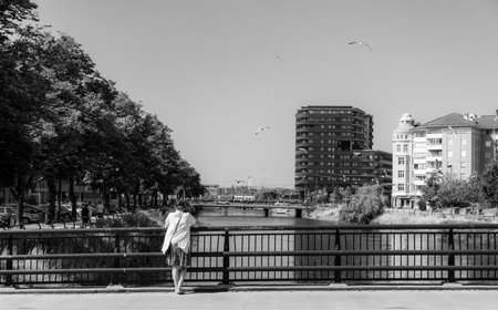 MalmÃ¶, Sweden - July 8, 2018: A lonely woman in her 50's is standing on a bridge over the canal looking at bypassing people. Monochrome.のeditorial素材