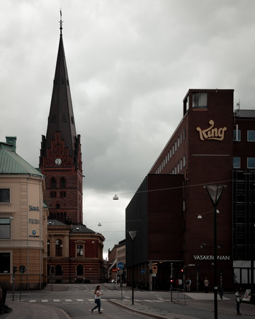 MalmÃ¶, Sweden - September 2, 2018: A woman crosses the street in downtown MalmÃ¶ with the St. Petri church and game developer King headquarters in the backgroundのeditorial素材