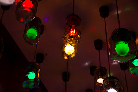 Some ceiling lights that consists of hanging glass jars with red and green colored light bulbs insideの写真素材