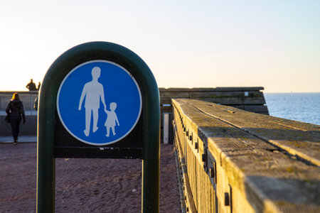 A Swedish walkway sign close to a pier. People walking in the background as the sun sets.の写真素材