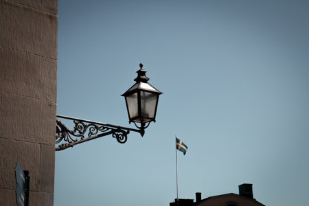 An old electric lamp mounted on a medieval building. The Swedish flag is visible in the backgroundの写真素材