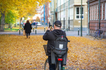 A man dressed in black stops with his bicycle to take photos of the fallen leaves and the yellow...