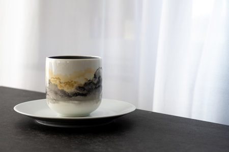 A coffee cup placed on a white saucer placed on a dark stone table with copy spaceの写真素材