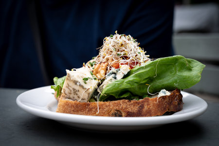 A delicious cheese sandwhich topped with walnuts, marmelade, and vegetablesの写真素材