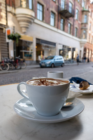 A fresh cup of hot chocolate of coffee in a white cup with saucer on streetside cafe tableの写真素材