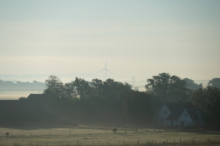 Landscape of foggy morning in SkÃ¥ne (Scania) showing flat farmlands and wind turbine generating renewable energyの写真素材