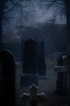 Dark and foggy cemetary with gravestones and crosses on a cold autumn dayの写真素材