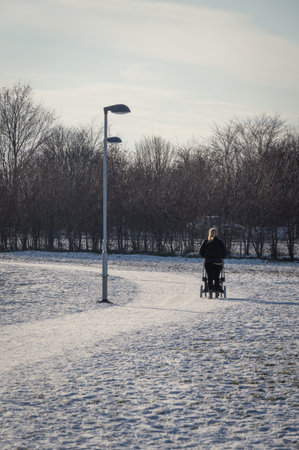 Woman walking with stroller in snow covered park during winter day in Swedenの写真素材