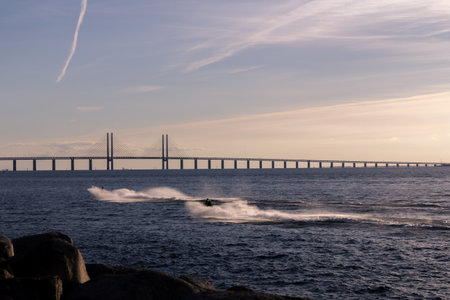 Two men racing on jetskis in the cold ocean in front of the Oresund bridge on a summer eveningの写真素材