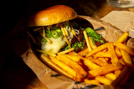 Cheeseburger with fries in paper on tableの写真素材