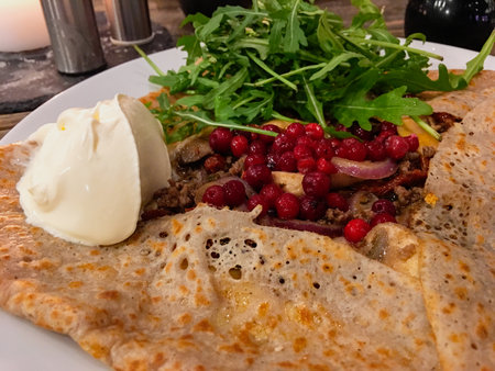 A crepe or galette filled with fried meat, mushrooms, lingonberry, rocket sallad and creme fraicheの写真素材