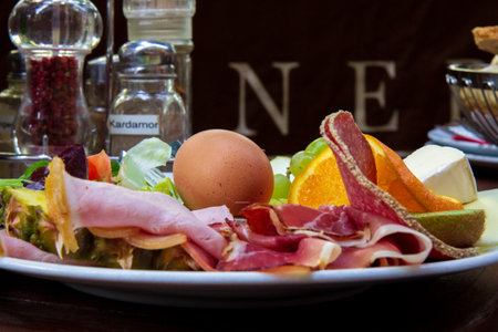 A plate of breakfast filled with egg, ham, sausage and fruitsの写真素材