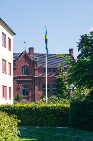 Swedish flag on flag pole in front of red brick building in summer timeの写真素材