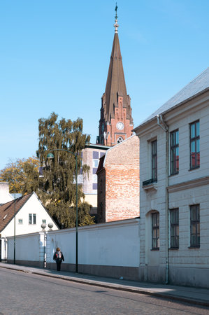 Woman walking along cobblestoned street in Lund Sweden with church Allhelgonakyrkan in the backgroundの写真素材