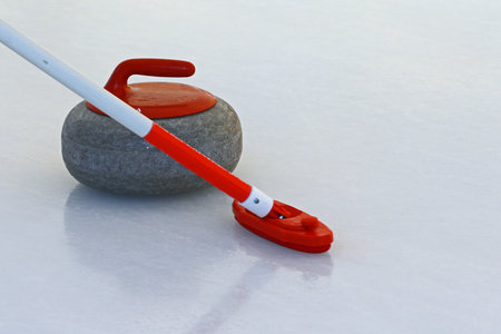 Curling stone and broom on the ice