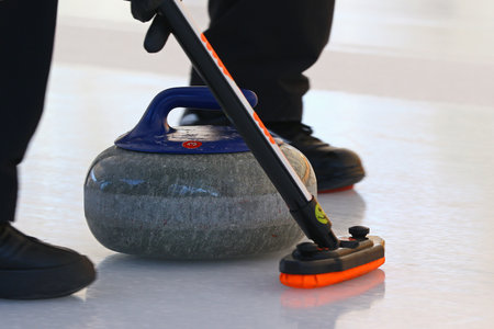 Curling stone sliding down the ice with player's feet running in front of itの写真素材