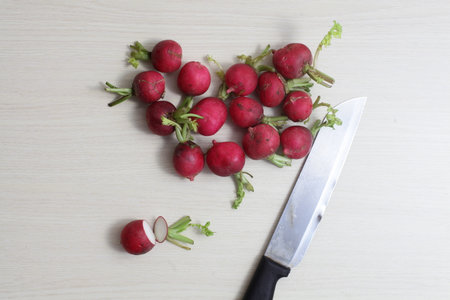 red radishes on wooden cutting board, with hand, knifeの写真素材
