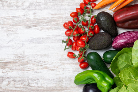 Fresh organic vegetables on white wood background. Healthy natural food on table with copy space. Carrots, cherry tomatoes, avocados, aubergines, zucchini, chard, red pepper, green pepper.の写真素材