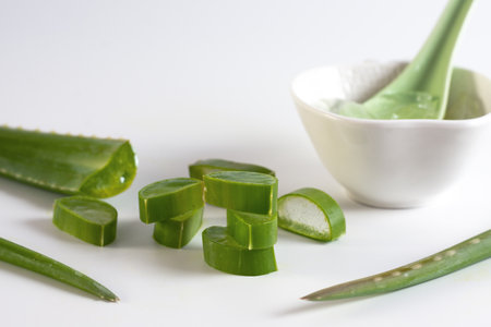 Sliced aloe vera and white jar with green spoon on white background, close viewの写真素材