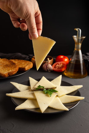 Hand catching a slice of cheese, plate slices of cheese with toast, oil, tomato, garlic. rustic dark backgroundの写真素材