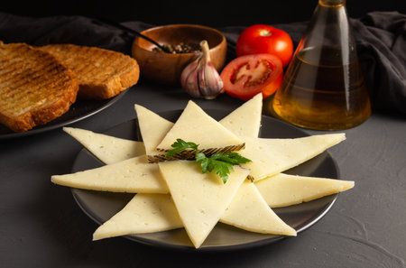 Sliced cheese plate with toast, oil, tomato, garlic. rustic dark background