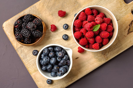 three bowls with wild berries, raspberry, blueberries, blackberries, on rustic wooden backgroundの写真素材