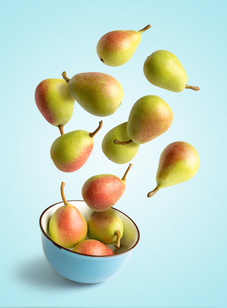 Small pears flying over a bowl, isolated from the blue background, concept of summer and healthの写真素材