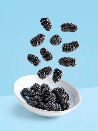 plate with blackberries flying on blue background