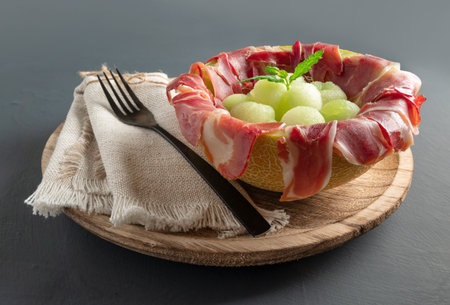 melon with air dried ham, served in halved melon stuffed with serrano ham and melon balls. on rustic wood backgroundの写真素材