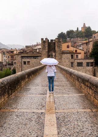 Woman with umbrella in the rain on a bridge in a medieval villageの写真素材